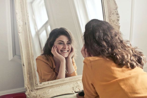 7 перевірених способів, як підвищити впевненість у собі 1 Жінка дивиться в дзеркало з посмішкою – як підвищити впевненість у собі
